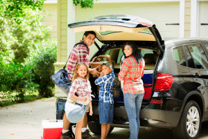 A happy family packs luggage into the trunk of their family car for a trip