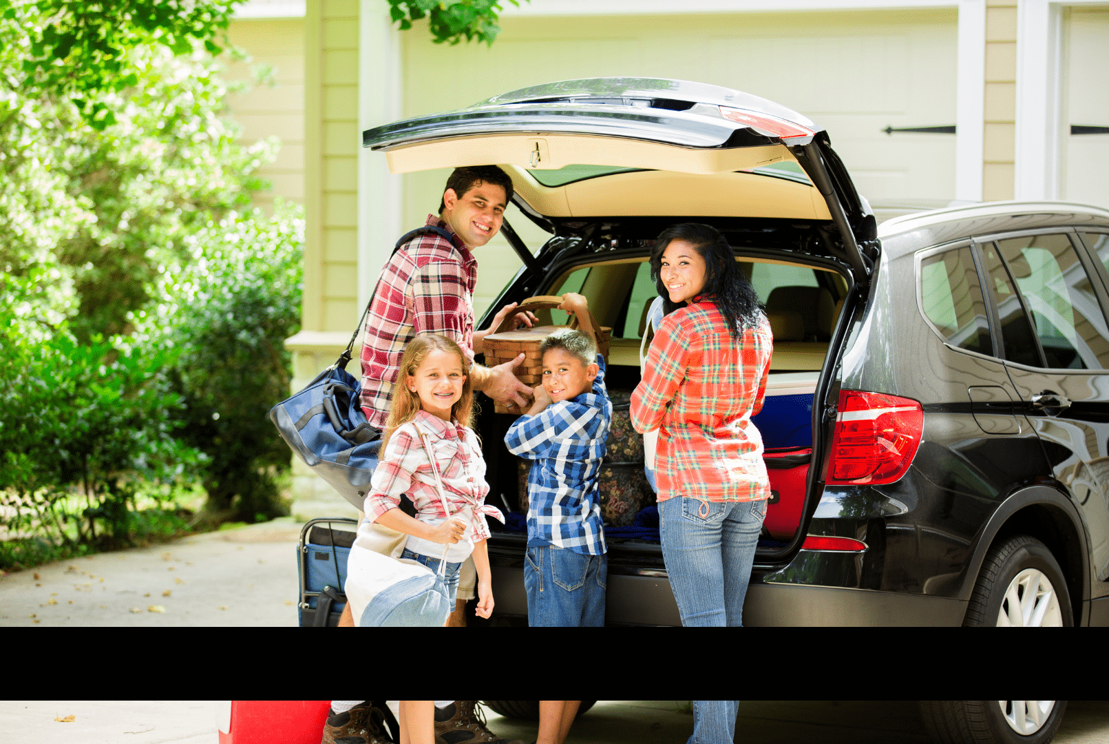 A happy family packs luggage into the trunk of their family car for a trip