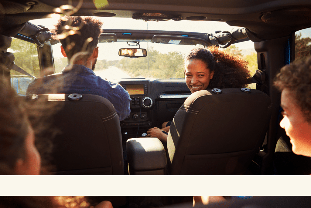 Inside a family car, a mother smiles at her children while the father drives