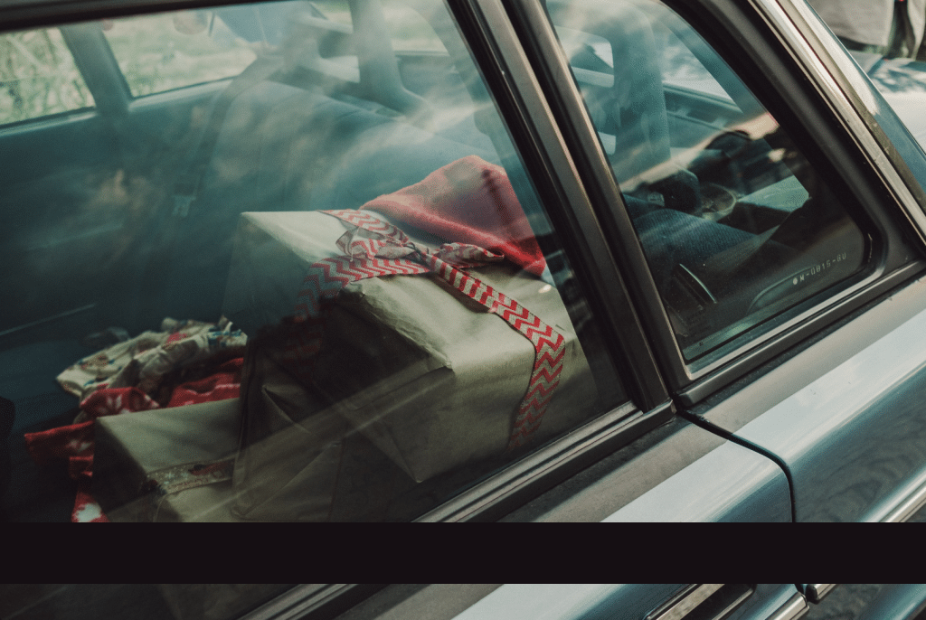 Wrapped gifts are stacked in the backseat of a family car, seen through the window